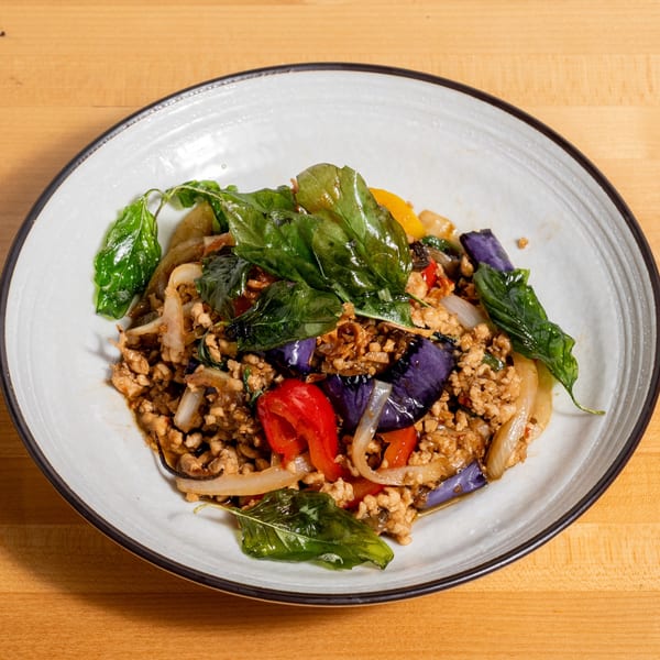 Stir-fried ground chicken with basil, eggplant, bell peppers, and onions on a white plate.