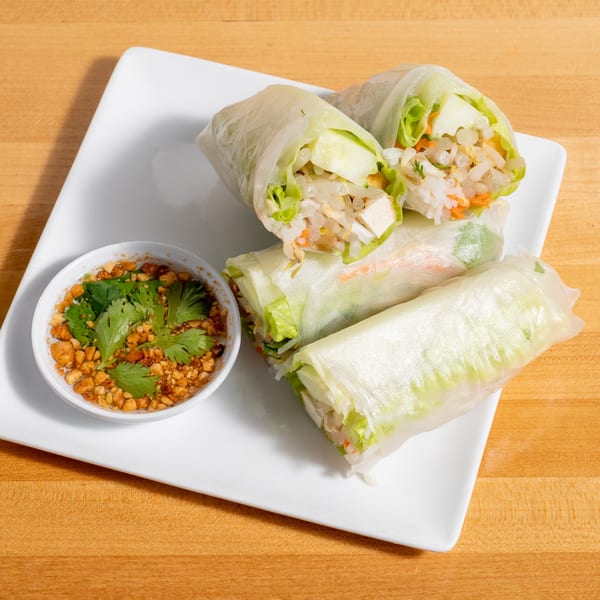 Four fresh spring rolls with tofu, rice, and vegetables, served with a peanut dipping sauce.