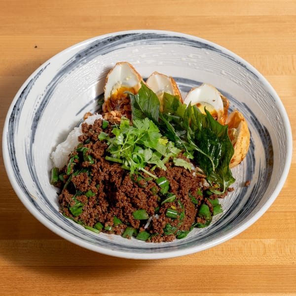 A bowl of rice topped with minced meat, green vegetables, cilantro, and fried eggs.