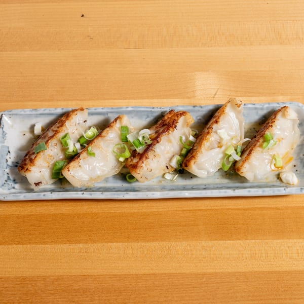 Five pan-fried dumplings with crispy bottoms and green onions on a rectangular plate.