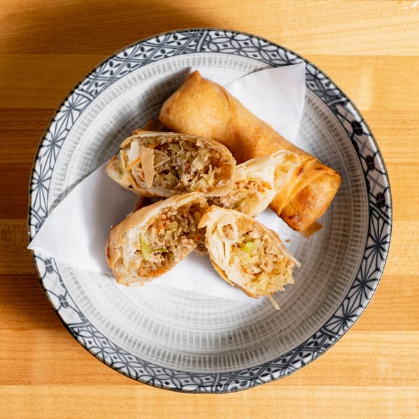 Crispy golden spring rolls, one whole and several cut open, revealing a savory filling in a patterned bowl.