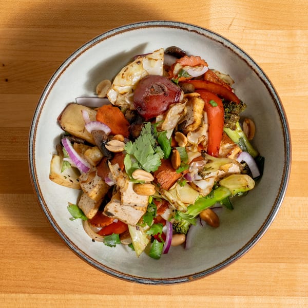 Overhead view of a colorful stir-fry with tofu, vegetables, and peanuts in a light gray bowl.