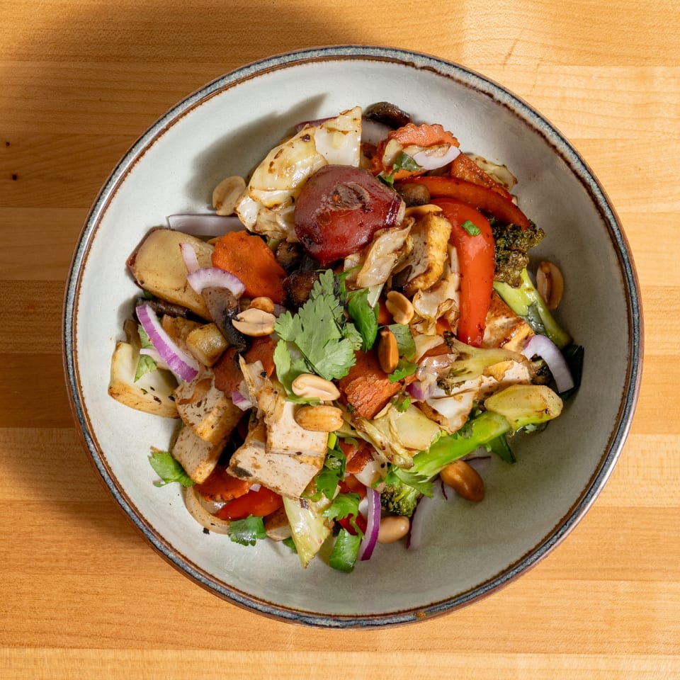 Overhead view of a colorful stir-fry with tofu, vegetables, and peanuts in a light gray bowl.